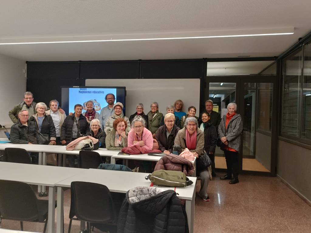 Un grup de persones somrients en una sala d'aula, amb un projector al fons mostrant el text 'Madalenus educatives'.